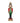 A festive nutcracker figurine standing on a decorated base, dressed in a red and green military-style coat with gold trim, black pants, and a black hat with gold detailing, set against a white bokeh background.