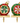 Two decorative Christmas tree ornaments displayed side by side on gold-colored stands against a white background. One ornament is red with green and white starburst detailing, and the other is green with red and pink starburst detailing, both featuring gold caps and loops.